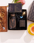 The Taurus Astrology Tea Gift Set offers a luxurious collection featuring a Taurus-themed tea blend, an elegant tea infuser, and precise measuring spoons displayed on a wooden tray decorated with loose tea leaves. Completing this celestial arrangement is a bright yellow teacup and saucer, alongside a black box adorned with star patterns.