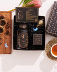 In a flat lay image of the Virgo Astrology Tea Gift Set, you can see a Virgo-themed bottle, two moon-shaped tea infusers, a box of Magic Hour full moon tea with organic ingredients, and a teacup with steeped tea, each item meticulously arranged on a white surface.