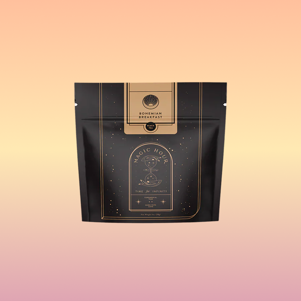 A black and gold resealable pouch labeled "Bohemian Breakfast Black Tea- Probiotic Rich Vanilla Puerh Tea for Digestion & Energy" by Magic Hour, with a celestial design, highlights this organic coffee alternative against a light pink background.