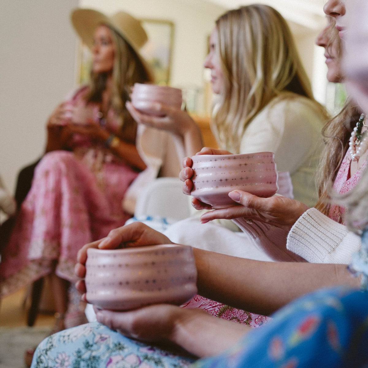 Four women gather for The Soul of Tea: A Two Day Retreat in Ojai, CA, each holding a pink ceramic bowl. Their softly blurred faces place emphasis on the bowls and their hands, while their pastel attire enhances the serene and tranquil ambiance of the tea ceremony.