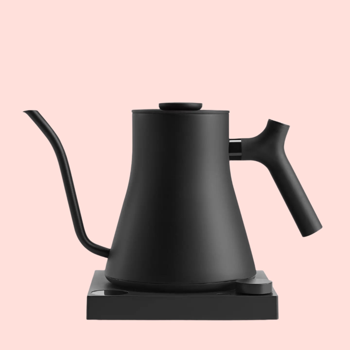 The Matte Black Pro Precision Electric Kettle, with customizable brew settings, a curved spout, and ergonomic handle, sits on its matching square base against a pale pink background.