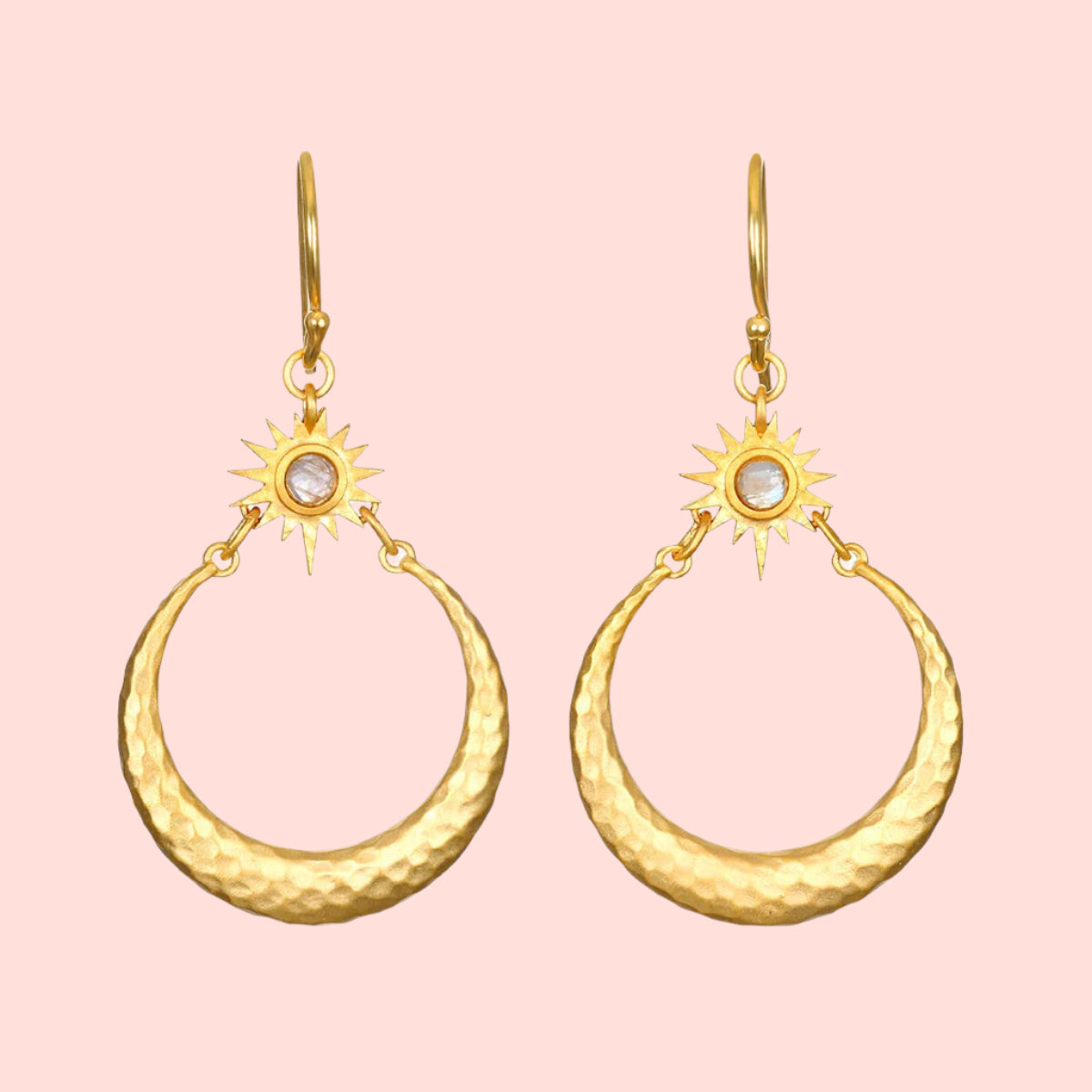 Introducing the Stellar Sisterhood Moonstone Hoops: gold earrings with hammered crescent shapes, sunburst designs, and small white moonstone centers, all elegantly hanging from gold hooks.