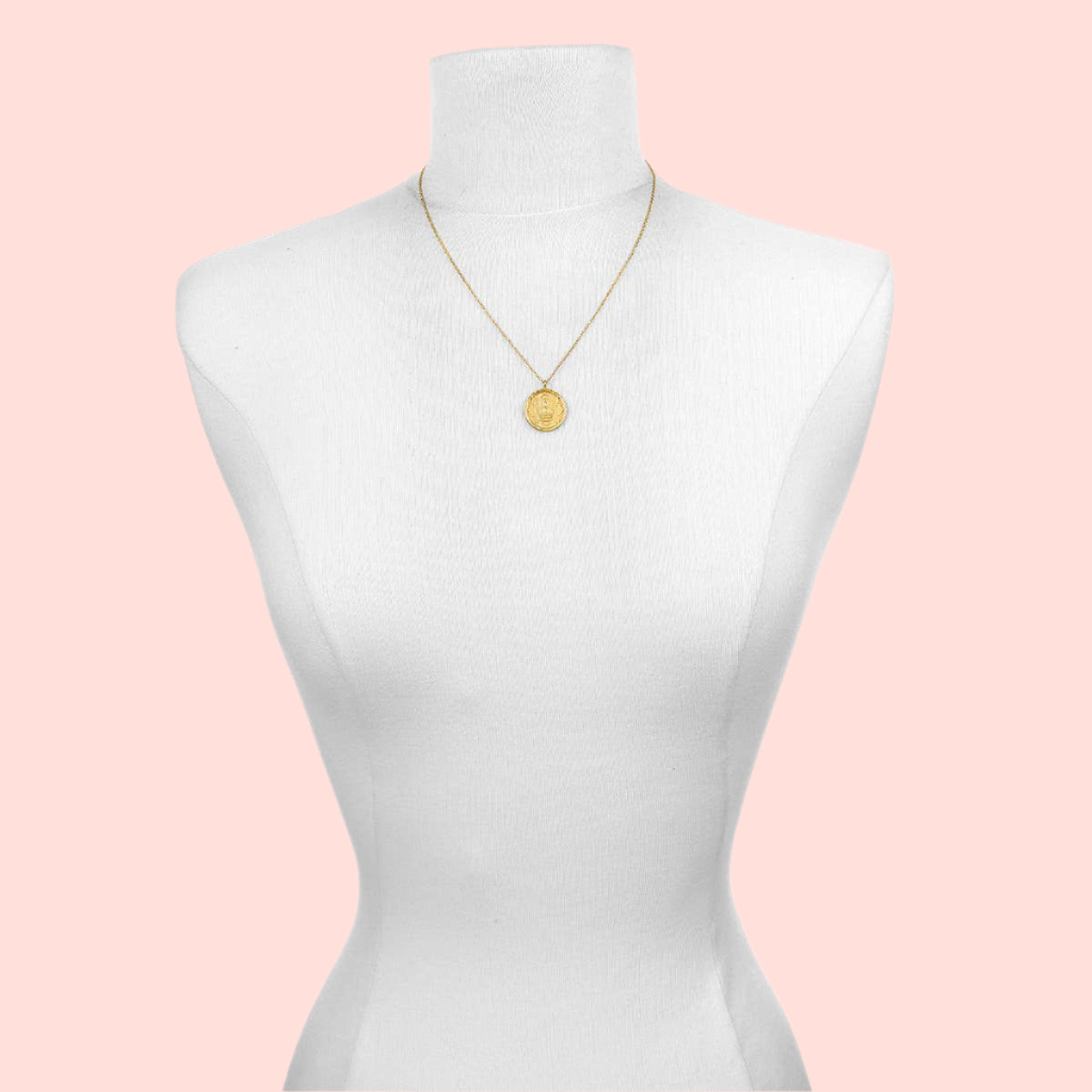 The Gold Buddha Pendant Necklace, featuring an 18kt gold plate, is shown on a white dress form mannequin. The pendant rests at chest level against a plain white background.