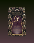 A black and gold package for the Monthly Magic Tea Journey Subscription features floral patterns, rare botanicals, and a goddess-like woman reaching upward inside a gold frame.