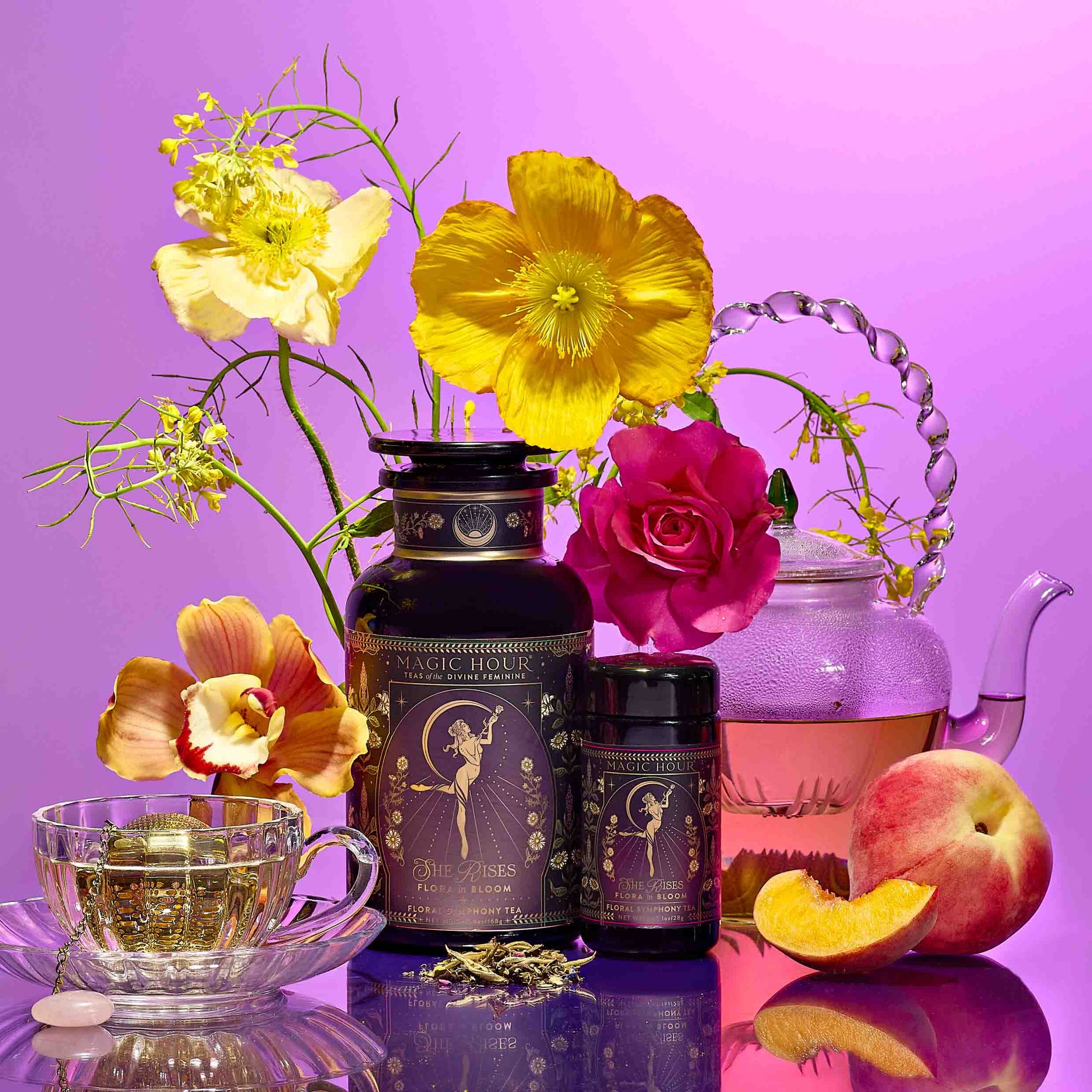 A vibrant still life with a glass teapot and teacup of pink tea, peach, yellow and pink flowers, goddess ritual tea canisters on a purple backdrop—perfect for Divine Feminine rituals or your Monthly Magic Tea Journey Subscription.