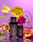 A vibrant still life with a glass teapot and teacup of pink tea, peach, yellow and pink flowers, goddess ritual tea canisters on a purple backdrop—perfect for Divine Feminine rituals or your Monthly Magic Tea Journey Subscription.