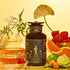 Freya: The Radiant tea set features a glass teapot and wellness tea cup beside a dark floral canister, surrounded by strawberries, orange slices, lime, kumquats, jasmine flowers, and a gold ginkgo leaf on a yellow background.
