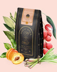A black and gold tea package labeled "Goddess Green Tea" is surrounded by illustrations of peaches, apricot lychee, lemongrass, green leaves, and small flower buds on a pale pink background.