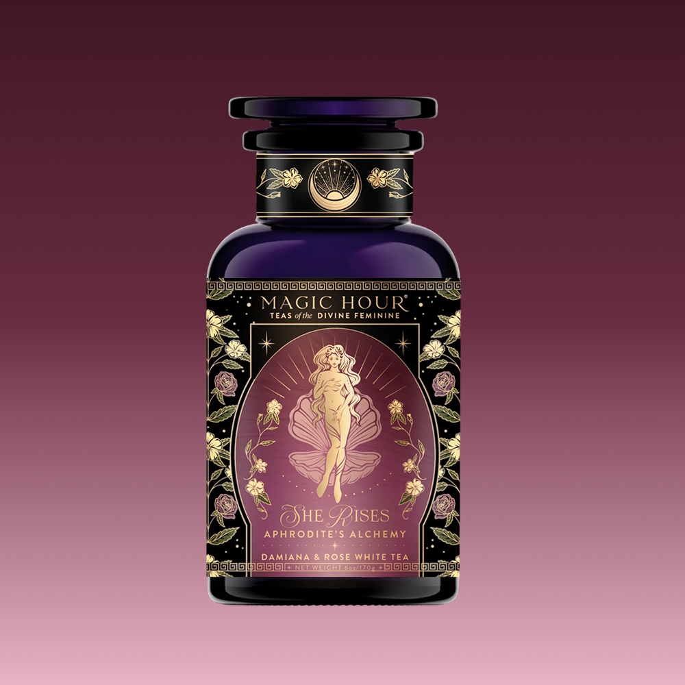 A beautifully designed tea package labeled "Aphrodite's Alchemy: Damiana &amp; Rose White Tea," featuring an illustrated goddess of love from Greek mythology, surrounded by flowers and elegant gold accents.