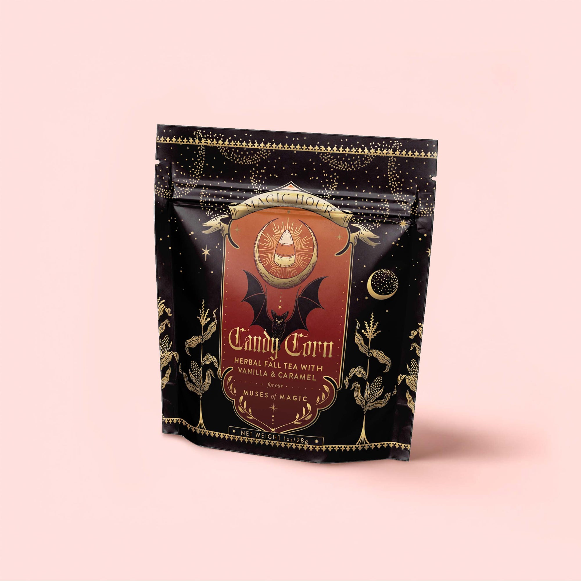 A black and gold package of Candy Corn: Herbal Fall Tea with Vanilla & Caramel, adorned with mystical designs, a bat, and plant illustrations, sits against a pale pink background. This caffeine-free blend is the ideal Halloween treat for anyone seeking the sweet taste of candy corn in every cozy sip.