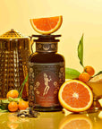 A tin of the Monthly Magic Tea Journey Subscription is surrounded by a gold teapot, orange slices, kumquats with leaves, loose tea, and a gold dish—all set against a yellow background—inviting you to discover the ritual guide inspired by goddess archetypes included with each enchanting tea subscription.