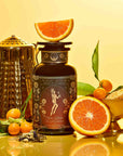 A gold teapot, a dark tea jar adorned with an illustrated label of Oshun’s Nectar: Honeyed Herbal Tea for Joy & Radiance, fresh oranges, kumquats, loose tea leaves, and a golden bowl with orange—all elegantly arranged on a yellow background—create an inviting tableau that captures the warmth and vibrancy of honeyed herbal tea.