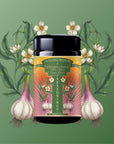 A jar of "Teasoning: Roasted Garlic Tea Salt" sits centered on a green background, framed by illustrated garlic bulbs and white flowers with leaves, capturing the savory essence of a garlic finishing salt.