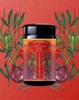 A black jar labeled “Teasoning: Chili Spice Rub” sits centered on a red background, surrounded by illustrated green and red chili peppers and purple onions with roots, highlighting its smoky Lapsang Souchong black tea seasoning.