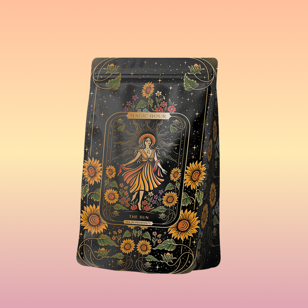 A dark amber bottle from Magic Hour, adorned with ornate label designs, features an illustration of a woman in a yellow dress surrounded by sunflowers and foliage. Titled "The Sun: Energizing Adaptogenic Herbal Tea with Yaupon, Moringa & Turmeric," the bottle has a black cap and displays intricate floral patterns with a mystical theme.