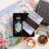 The Travel to Tulum Gift Set includes a tea jar, pastel cloth, and "Magic Hour" box. Experience the unique Tulum Horchata Chai with its loose leaves on floral-themed paper against a vibrant backdrop for an enchanting tea moment.