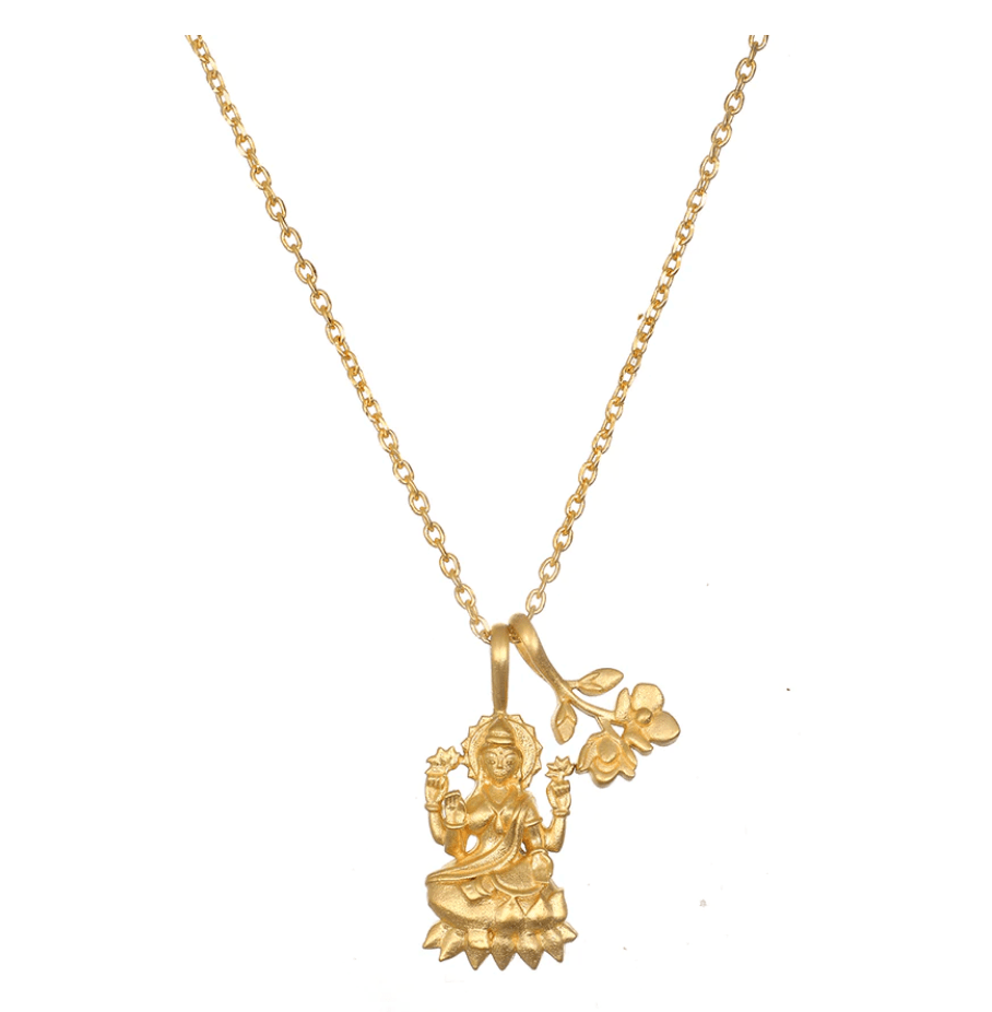 The Lakshmi Hindu Goddess, Awaken Abundance Necklace- ARCHIVE showcases a gold pendant depicting a seated figure with a lotus base, holding flowers, and accompanied by a small floral charm. The pendant is elegantly suspended from a delicate chain.