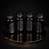 Four dark glass bottles with decorative labels stand on a golden tray against a dark background. The intricate designs read "Weight No More - Luxury Slimming Teas of the Far East," hinting at an elegant tea ceremony. One bottle, marked with a green label accent, suggests detoxifying qualities, while the others remain uniformly black.
