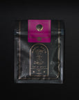 A black-colored Magic Hour Tea package is shown against a dark background. The bag has a decorative gold design with an hourglass illustration, and it reads "Time for Infinity." A pink label with a circular emblem that says "Soulmate: Chocolate-Raspberry-Rose Black Tea for Finding & Celebrating Love" is attached at the top, highlighting its organic loose leaf tea inside.