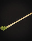 A Ceremonial Matcha Bamboo Scoop by Magic Hour sits on a dark background with some matcha powder on the scoop's end. The green of the matcha contrasts sharply with the dark setting, emphasizing its vibrant color—perfect for enjoying your Magic Hour moment.
