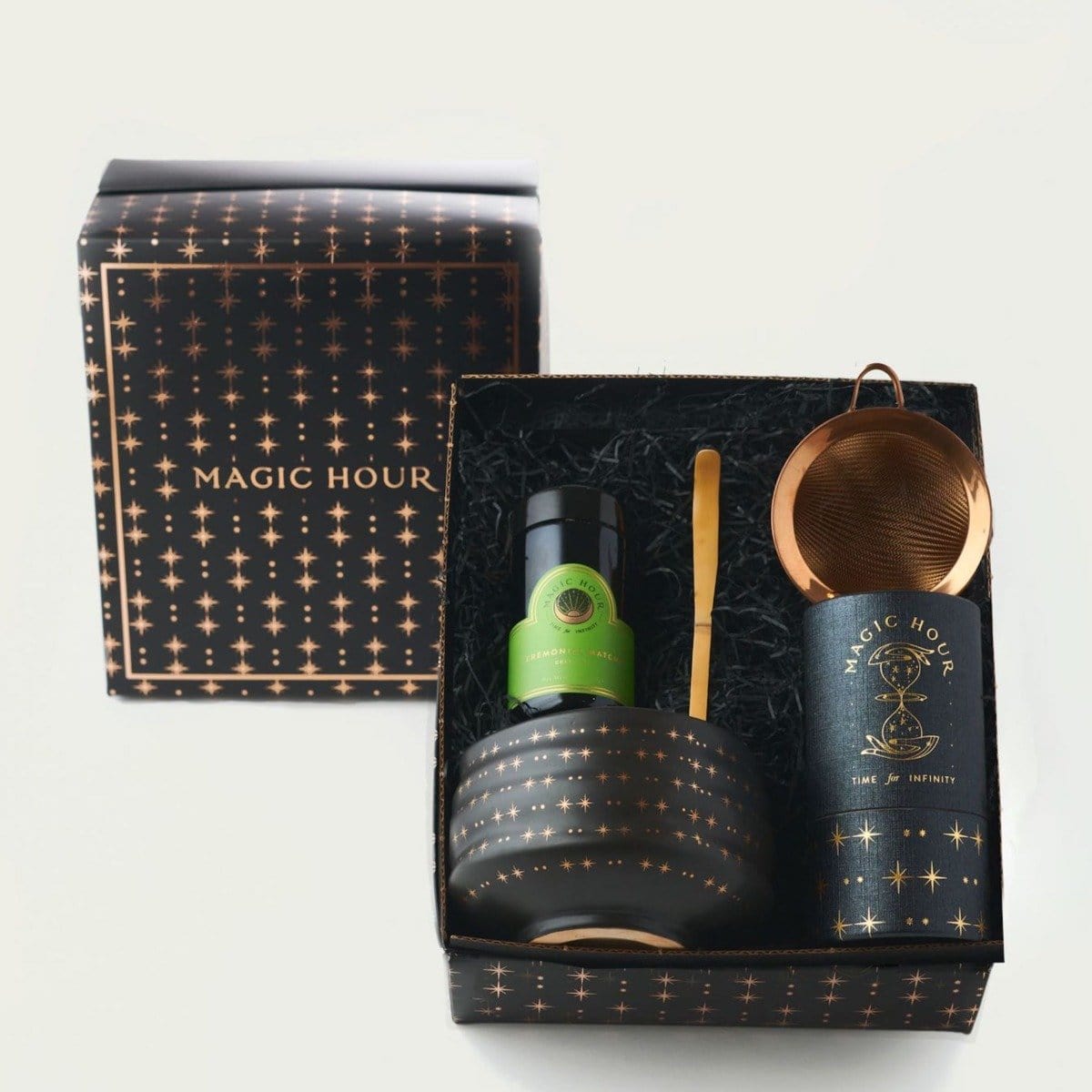 Ceremonial Matcha Traveler Gift Box with a "Magic Hour" theme. Includes a tin of loose leaf tea, green tea bottle, golden tea spoon, black tea bowl with metallic dots, and copper tea strainer. Set is displayed in a black box with a starry pattern.