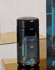 A black cylindrical container with a blue geometric design sits on a golden reflective shelf. The label reads "Magic Hour" with "Aquamarine Dream - Soothing Herbal Ayurvedic Adrenal Tonic" written below. This loose leaf tea is flanked by a similar design on the right, adding to the allure of Magic Hour Tea.