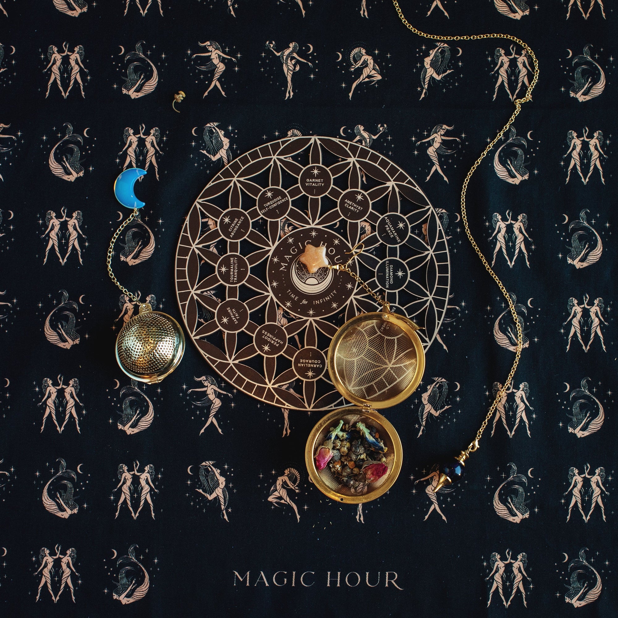 A mystical setup featuring a geometric and lunar phase chart, a gold locket holding various crystals, and a moon-shaped pendant, all set on a celestial-patterned cloth with dancing figures. A steaming cup of loose leaf tea completes the scene. The caption at the bottom reads "Magic Hour Tea Ceremony Towels.