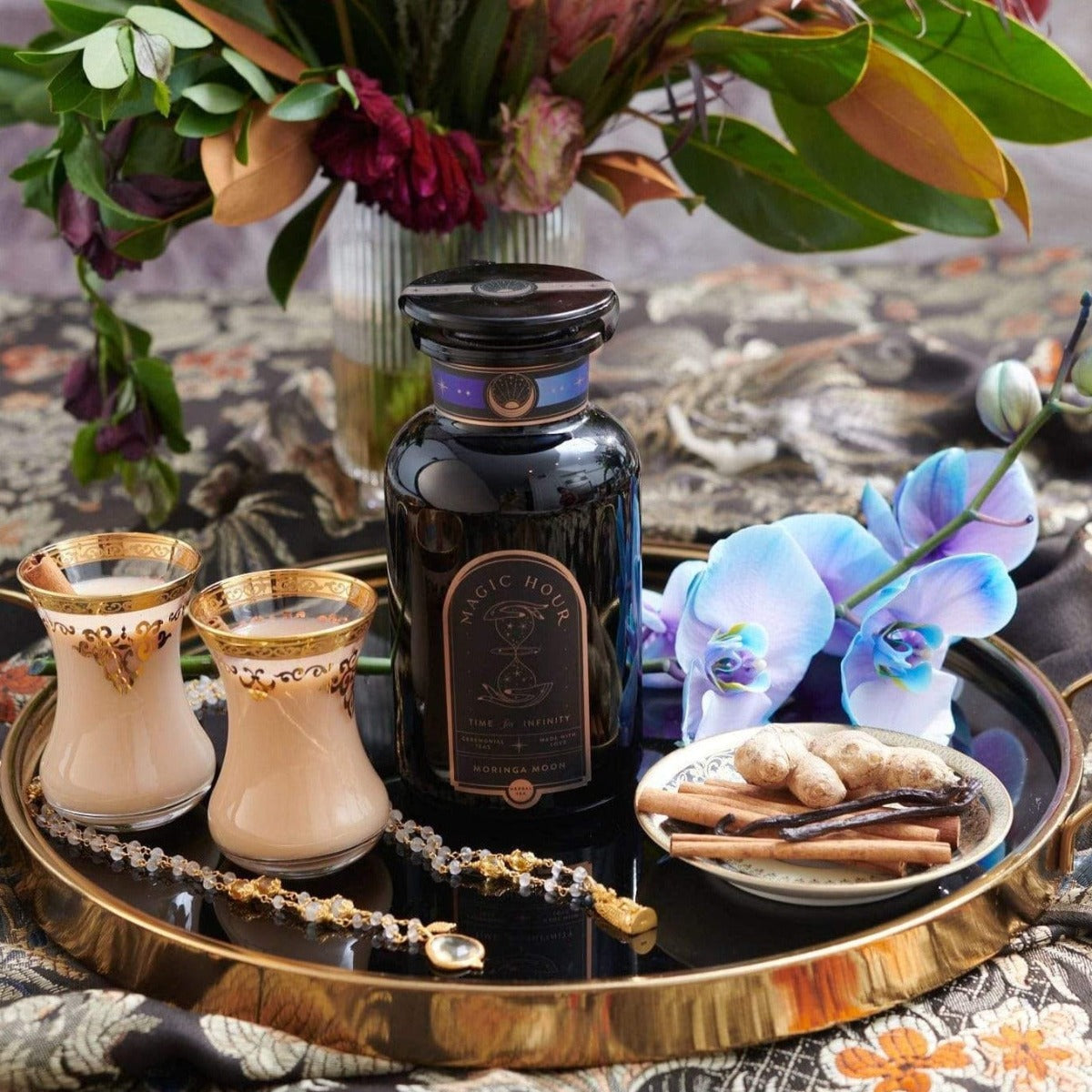 Arranged tea set with bottle, flowers, and decorative items on a satin cloth.