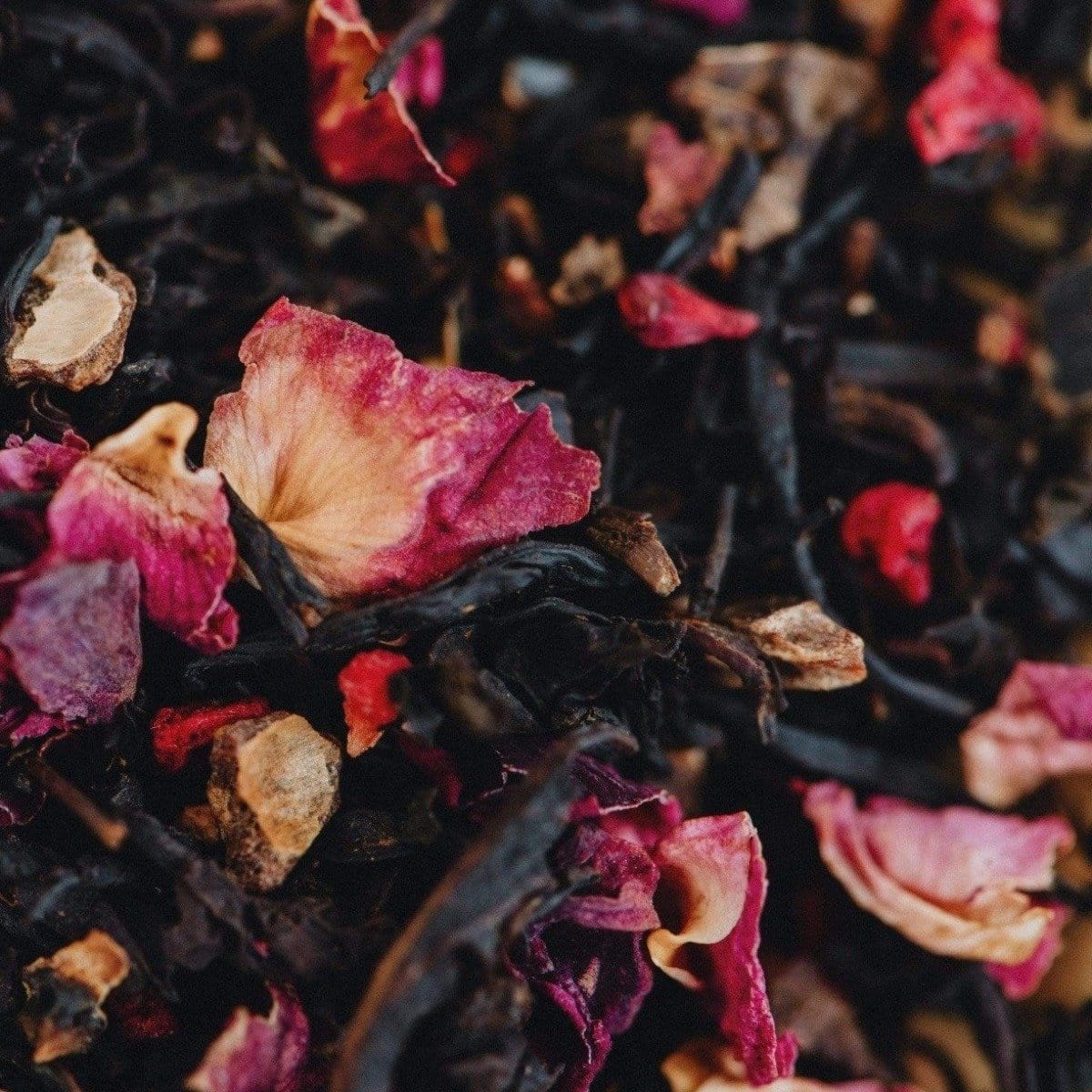 A close-up image of a blend of dried organic tea leaves mixed with vibrant pink and red rose petals, creating a colorful and textured composition. The varied shapes and hues of the petals contrast beautifully with the dark leaves in Magic Hour&#39;s Soulmate: Chocolate-Raspberry-Rose Black Tea for Finding &amp; Celebrating Love.